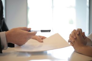 An image showing an intellectual property lawyer passing a client some papers to sign, regarding the protection of their intellectual property.
